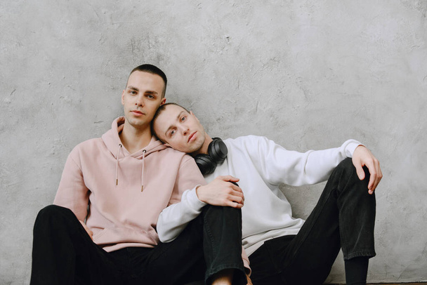 Young gay couple sitting on floor using laptop, using headphones listen to music together, hugging or embracing. - Fotó, kép