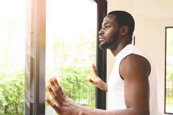 Портрет задумчивого афроамериканца, стоящего, трогательного и смотрящего в окно дома - Фото, изображение