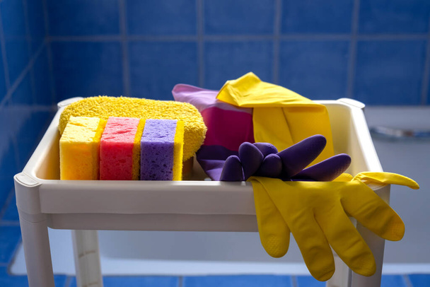 Λαστιχένια γάντια και σφουγγάρια σε λευκό ράφι στο εσωτερικό μπάνιο. Κοντινό πλάνο. Σύνολο πολύχρωμα αξεσουάρ για τον καθαρισμό του σπιτιού. Καθαρό σπίτι. Πρόσθια όψη. - Φωτογραφία, εικόνα