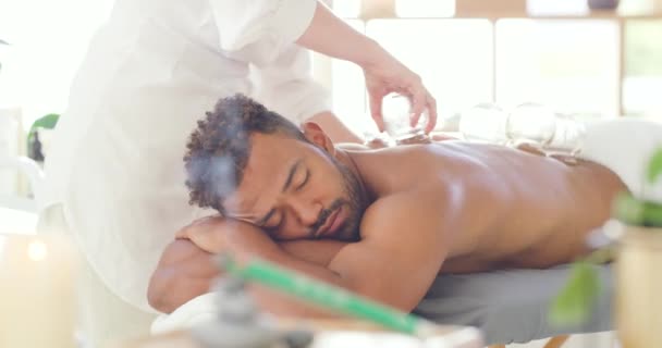 Young man enjoying relaxing and therapeutic back massage treatment with vacuum cups in a spa. Beauty therapist treating muscle pain with suction cupping therapy to remove body toxins. - Footage, Video
