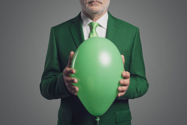 Confident corporate businessman holding a green balloon, ecology and sustainable business concept - Foto, Imagen