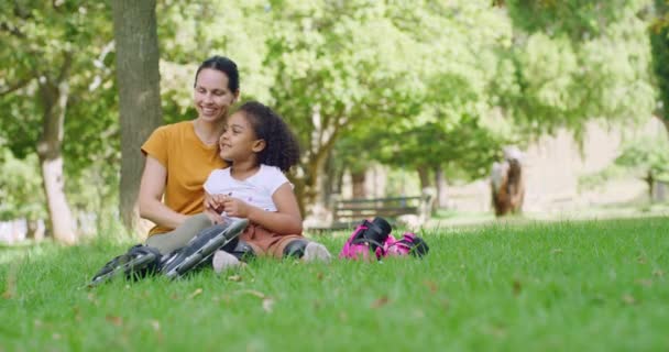 Szczęśliwa matka i jej urocza adoptowana córka relaksująca się i rozmawiająca na trawie w parku publicznym w słoneczny dzień. Uśmiechnięta kobieta i mała córeczka łączą się i dzielą czułym pocałunkiem w ogrodzie. - Materiał filmowy, wideo