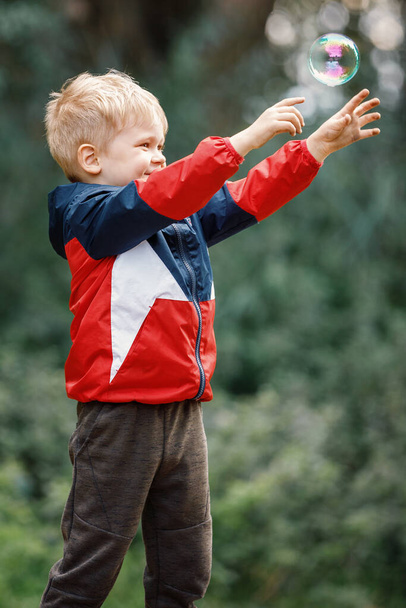 Very happy kid trying to catch soap bubble. - Foto, Imagen