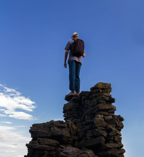 Fiatal fehér férfi hátizsákkal, kőből összehajtogatott sziklán áll. Cseh nyári táj, természetvédelmi terület Slepici hory - Fotó, kép