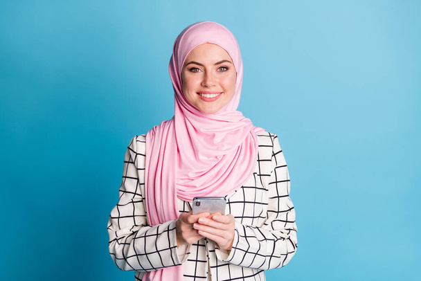Portrait of pretty cheerful muslimah girl using device browsing post multimedia free time isolated over bright blue color background. - Foto, Imagen