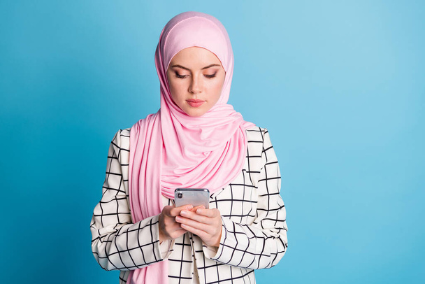 Portrait of pretty serious focused muslimah girl using device gadget chatting isolated over bright blue color background. - Фото, зображення