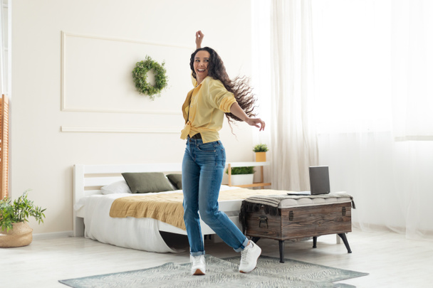 Full length of happy young woman dancing and having fun at home, copy space. Cheerful millennial lady moving to favorite soundtrack, enjoying music on laptop in bedroom - Fotoğraf, Görsel
