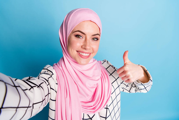 Self-portrait of pretty cheerful glad muslimah girl showing thumbup advert advice isolated over bright blue color background. - Foto, immagini
