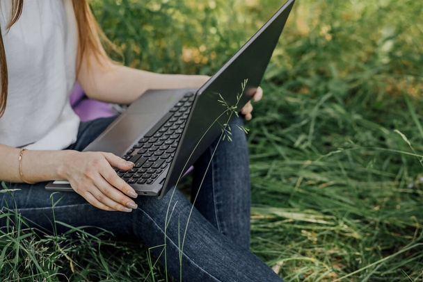 chica se sienta en la hierba y trabaja en un ordenador portátil. freelance - Foto, Imagen