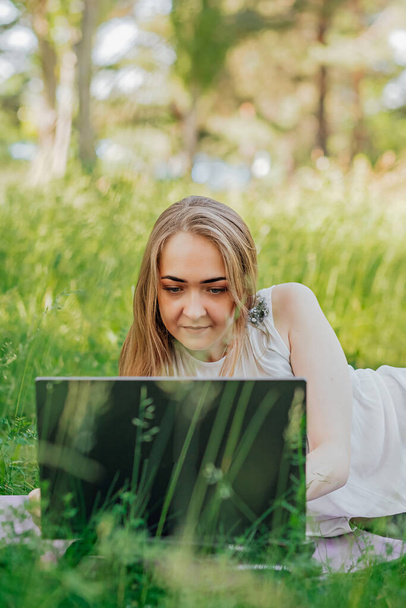 the girl sits on the grass and uses a laptop. Education, lifestyle, technology concept, outdoor learning concept. - Photo, Image