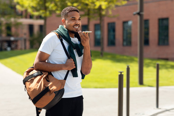 Όμορφος Αφροαμερικάνος που χρησιμοποιεί εικονική φωνητική βοηθό σε smartphone ή ηχογράφηση ηχητικού μηνύματος, περπατώντας στην αστική περιοχή της πόλης. Άνθρωπος που απολαμβάνει τις σύγχρονες τεχνολογίες επικοινωνίας - Φωτογραφία, εικόνα