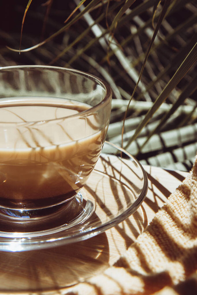 Üvegpohár illatos cappuccino kávé egy nyári veranda hátterében pálmafák - Fotó, kép