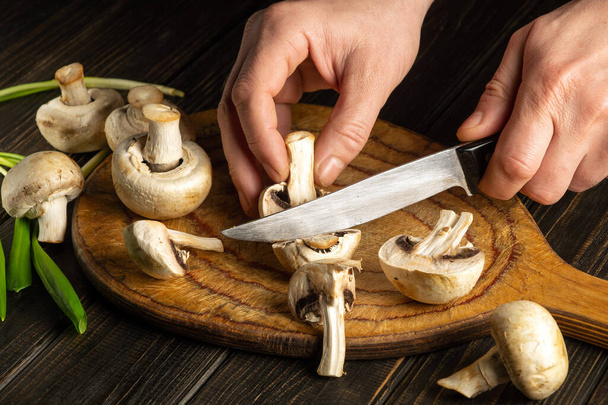 A séf gombát vág a vágódeszkán. Agaricus gombát főz a szakács keze által a konyhában. - Fotó, kép