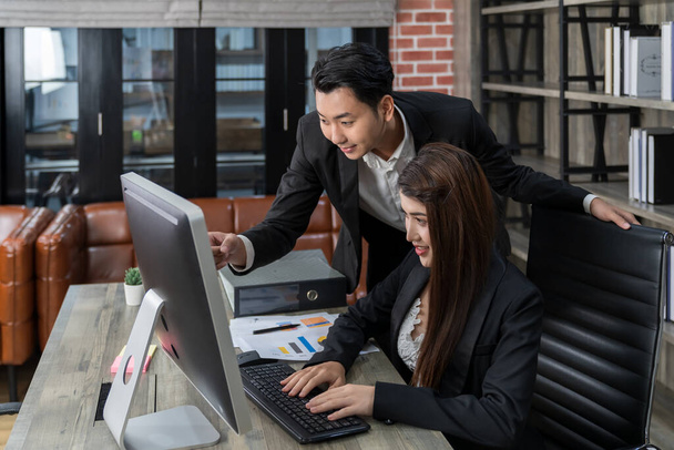 standing businessman officer helping sitting female worker with her computer works in office. teamwork concept. happy Asian business people working together. - Foto, Bild
