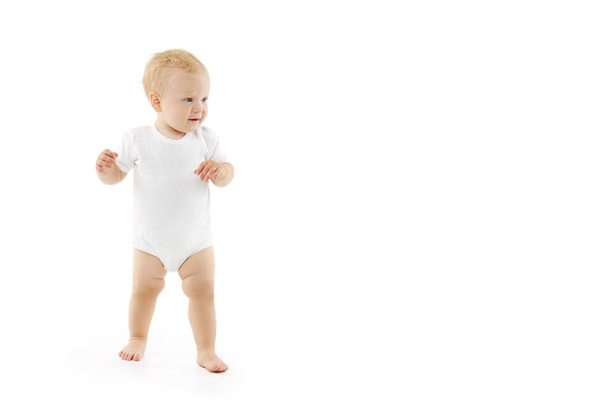Cute baby learns to walk on a white isolated background. Happy smiling child in white clothes makes first confident steps - Foto, immagini