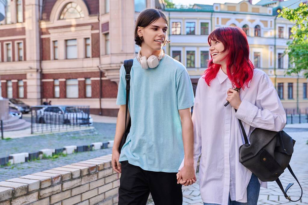 Couple of happy teenage friends walking holding hands, outdoor, on city street. Friendship, romantic, youth, leisure, relationship, lifestyle concept - 写真・画像