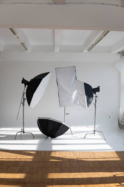 Professional lighting equipment, flashes, c-stands on a cyclorama in modern photo studio with a huge windows. Octabox, stripbox, softbox, buety plate and other stuff for photography - Fotoğraf, Görsel