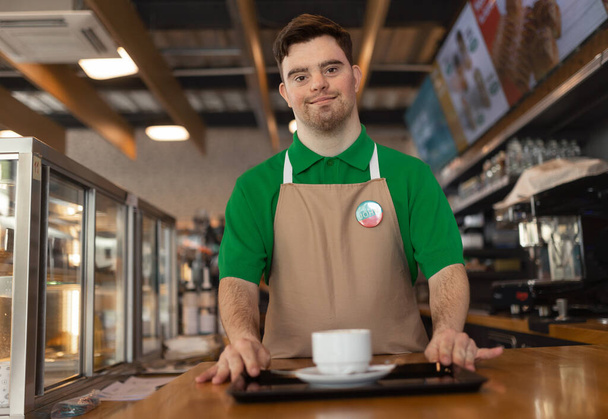 Un camarero feliz con síndrome de Down llevando café al cliente en la cafetería de la gasolinera. Concepto de inclusión social. - Foto, imagen
