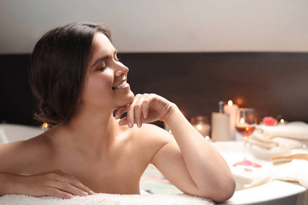 Happy beautiful woman taking bath with flower petals indoors. Romantic atmosphere - Fotó, kép