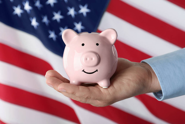 Woman holding piggy bank against American flag, closeup - Foto, afbeelding