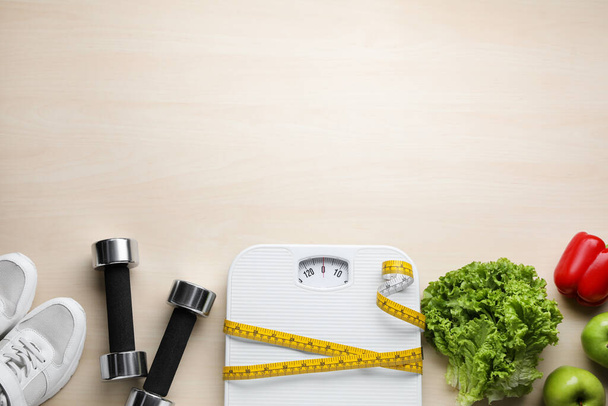 Flat lay composition with bathroom scale and measuring tape on wooden floor, space for text. Weight loss concept - Foto, imagen