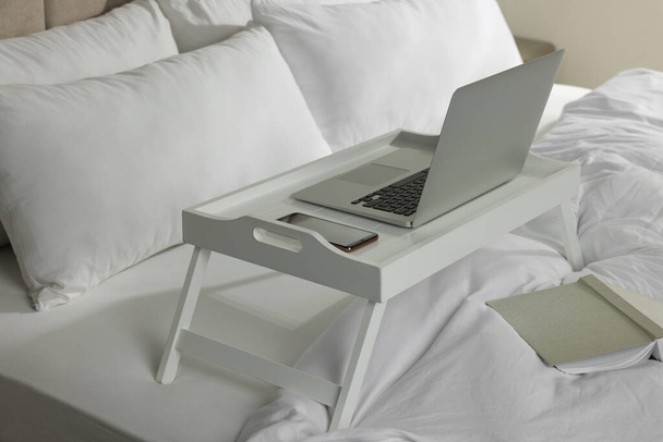 White tray with modern laptop and smartphone on bed indoors - Valokuva, kuva