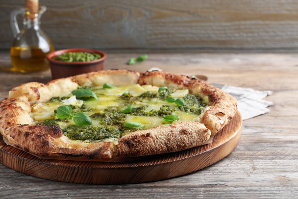 Delicious pizza with pesto, cheese and basil on wooden table - Foto, imagen