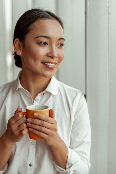 Retrato de mulher de negócios asiática bebendo café em pé perto de janelas no escritório. Foto de alta qualidade - Foto, Imagem