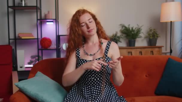 Call me, here is contact number. Redhead young woman looking at camera advertising doing phone gesture like says hey you call me back at home apartment. Ginger cute girl in living room sitting on sofa - Filmati, video