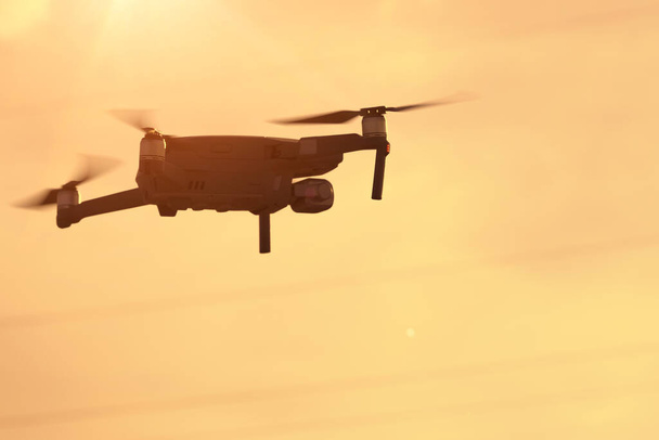 Квадрикоптер летит прямо на закате, современный квадрокоптер взлетает в воздух - Фото, изображение
