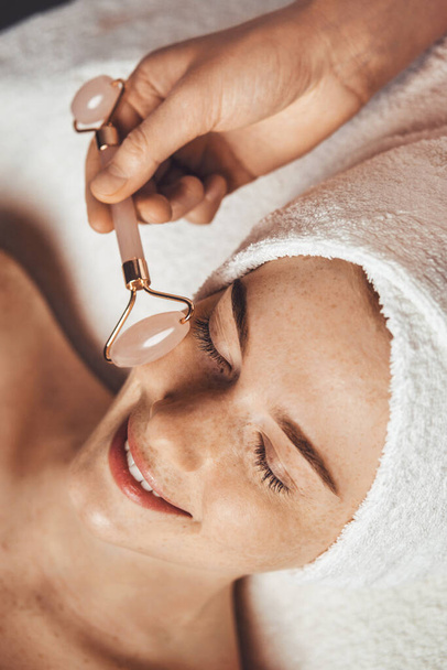 Patient receiving anti-aging face massage with jade roller face massager at spa salon. Beauty skin. Beauty face. Beauty treatment. Skin care. - Fotó, kép