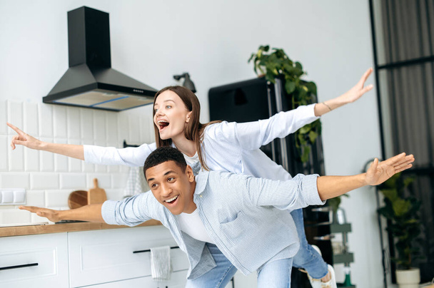 Multiracial happy couple in love, caucasian girl and latino guy, dressed in a modern casual clothes, have fun together at home in the kitchen, laugh, enjoy the weekend, experiencing positive emotions - Foto, Bild