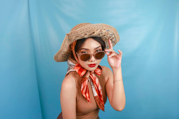 Young Asian confident and happy woman holding her sunglasses isolated by a blue background. - Foto, afbeelding
