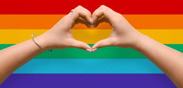 Woman making heart shape with her hands on rainbow background. LGBT concept - Foto, imagen
