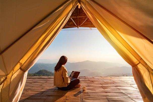 Young woman freelancer traveler working online using laptop and enjoying the beautiful nature landscape with mountain view at sunrise - Foto, Imagem