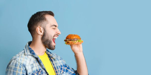 Young man eating tasty burger on light blue background with space for text - Foto, Bild