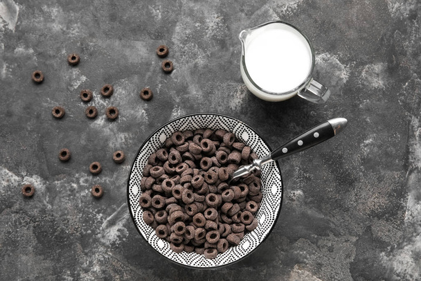 Bowl with black cereal rings and jug of milk on dark background - Fotoğraf, Görsel