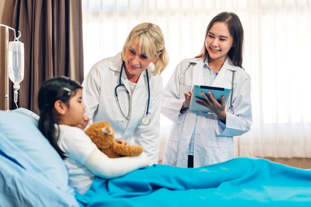 Asian smiling woman doctor service help support discussing and consulting talk to little girl patient give teddy bear and check up information in hospital - 写真・画像