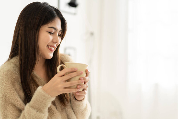 Portrait of smiling happy cheerful beauty pretty asian woman relaxing drinking and looking at cup of hot coffee or tea.Girl felling enjoy having breakfast in holiday morning vacation on bed at home - Fotoğraf, Görsel