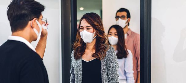 Bir grup profesyonel Asya işi ve ofiste koruyucu maske takarak koronavirüs için karantinada çalışmadan önce vücut ısısını ölçmek için kızılötesi termometre kullanılıyor. - Fotoğraf, Görsel