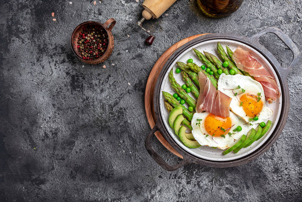 Tasty breakfast. avocado, asparagus, jamon, ham, prosciutto and fried egg on white plate. Ketogenic diet. Low carb high fat breakfast, top view. - Foto, afbeelding