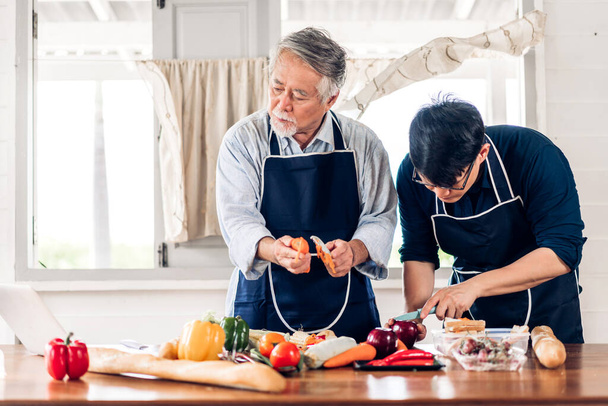 Портрет счастливой любви азиатской семьи старший зрелый отец и молодой взрослый сын весело готовить вместе и ищет рецепт в Интернете с ноутбуком, чтобы подготовить вкусный обед еды - Фото, изображение
