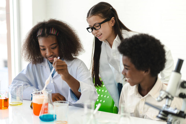 Группа студентов-подростков учится и учится, проводя химический эксперимент и держа в руках пробирку в лабораторном классе эксперимента на столе в школе. - Фото, изображение