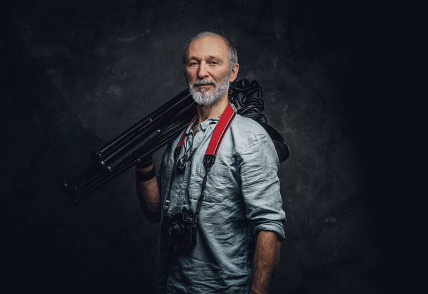 Shot of stylish elderly man photographer with photocamera holding spotlights on his shoulder. - Photo, Image