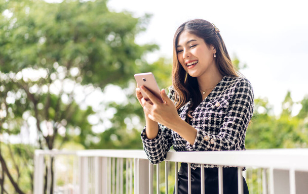 Portret van lachende gelukkige mooie Aziatische vrouw ontspannen met behulp van digitale smartphone.Young aziatische meisje kijken naar het scherm typen bericht en het spelen van spel online of sociale media in de stad - Foto, afbeelding