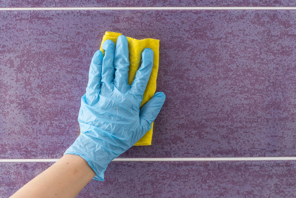 Υπάλληλος χέρι σε ελαστικό προστατευτικό γάντι με μικρο ίνες πανί σκουπίσματος τοίχο από τη σκόνη. Υπηρέτρια ή νοικοκυρά νοιάζεται για το σπίτι. Άνοιξη γενική ή τακτικό καθαρισμό. Εμπορική καθαρισμού εταιρεία έννοια. - Φωτογραφία, εικόνα