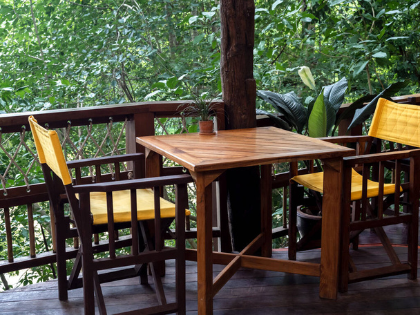 Leerer hölzerner Esstisch mit gelben Stühlen auf den Holzterrassenböden auf grünem Dschungel-Hintergrund. - Foto, Bild