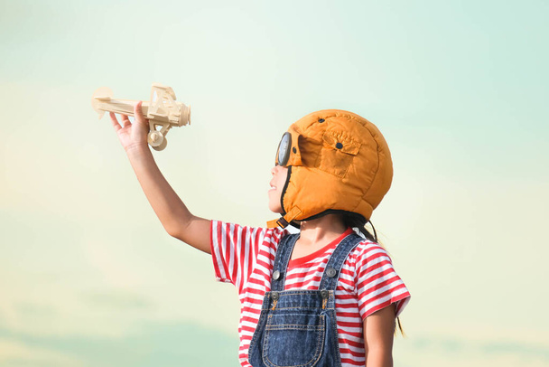 Schattig klein meisje spelen met speelgoed vliegtuig tegen pastel lucht achtergrond. Gelukkige jongen met een pilotenmuts die met een speelgoedvliegtuig speelt in het zomerpark. Jeugd droom fantasie concept. - Foto, afbeelding