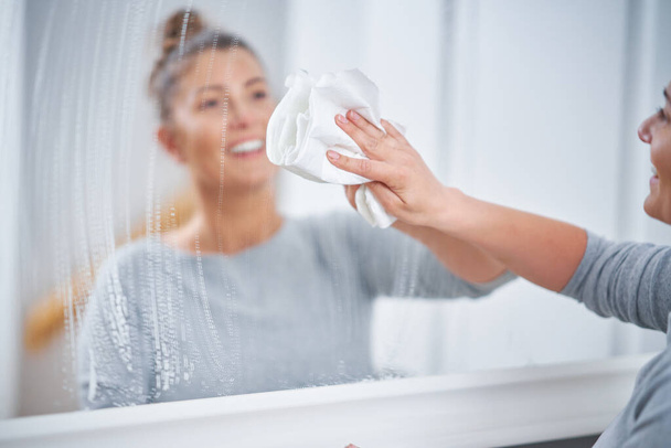 Imagen de una mujer yound limpiando la ventana del espejo. Foto de alta calidad - Foto, Imagen