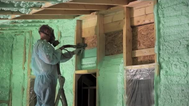 Мужчина-строитель изолирует деревянный каркасный дом. Работник, распыляющий пену полиуретана внутри будущего коттеджа, с помощью пистолета с множественными компонентами. Концепция строительства и изоляции. - Кадры, видео